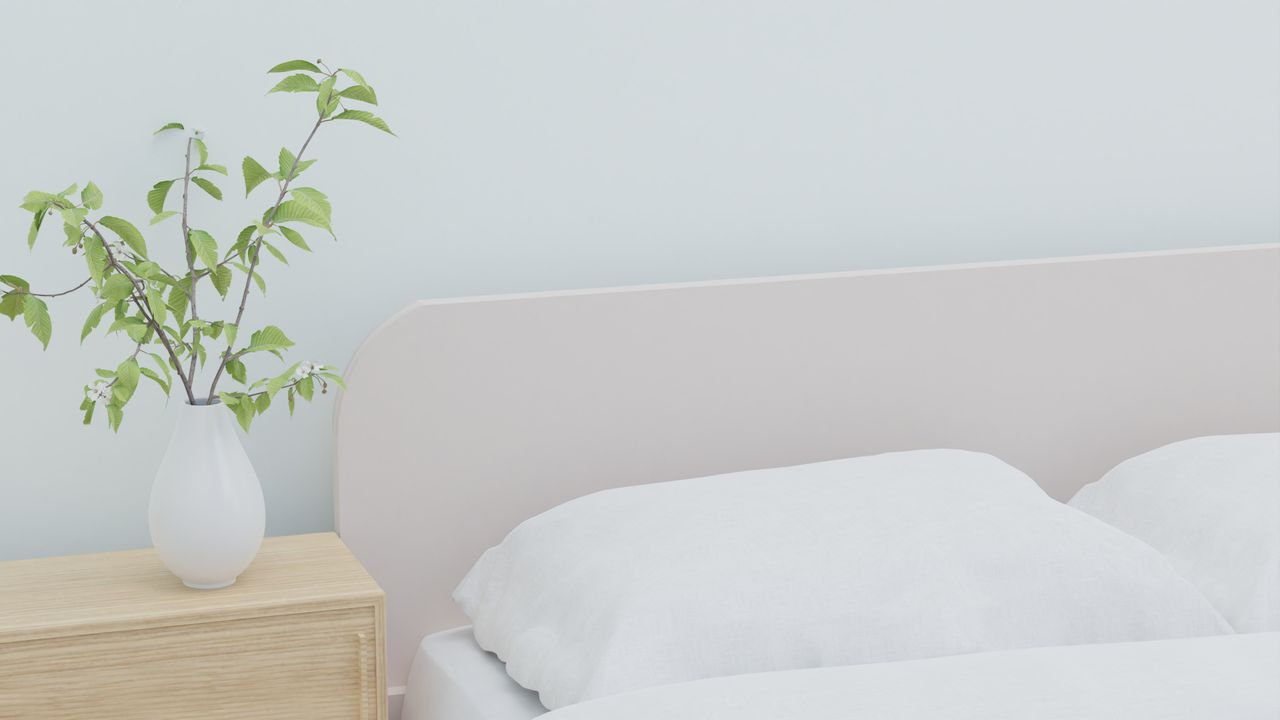 Soft and serene bedroom featuring white bedding and a vase with greenery on a wooden nightstand.